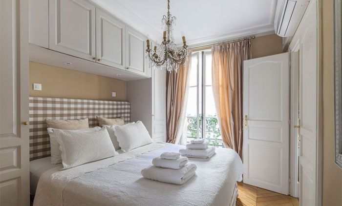 A bedroom in a Paris apartment with a white bed and a chandelier.