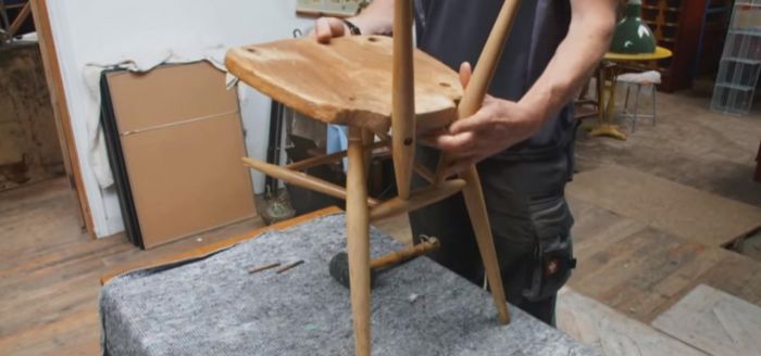 A man is working on a wooden chair for his home DIY project in a workshop.