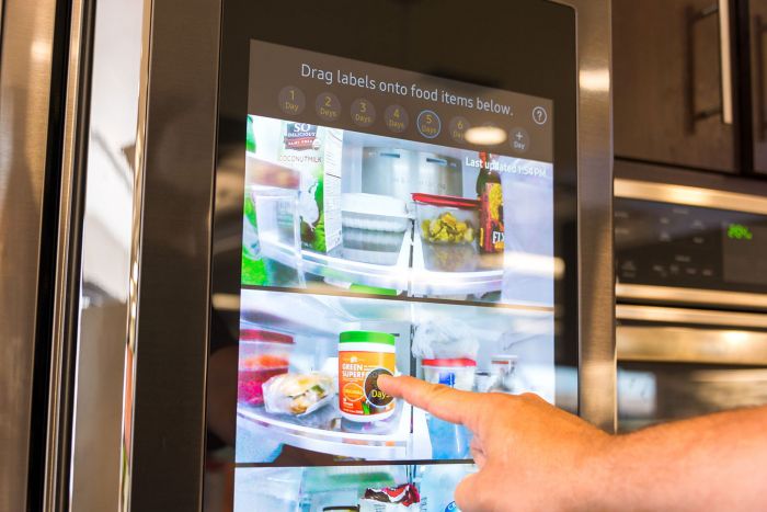 A person pointing at a screen displaying kitchen designs in a refrigerator.
