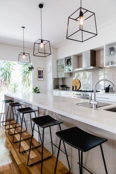 A white kitchen with black stools and wooden floors featuring kitchen island and lighting.