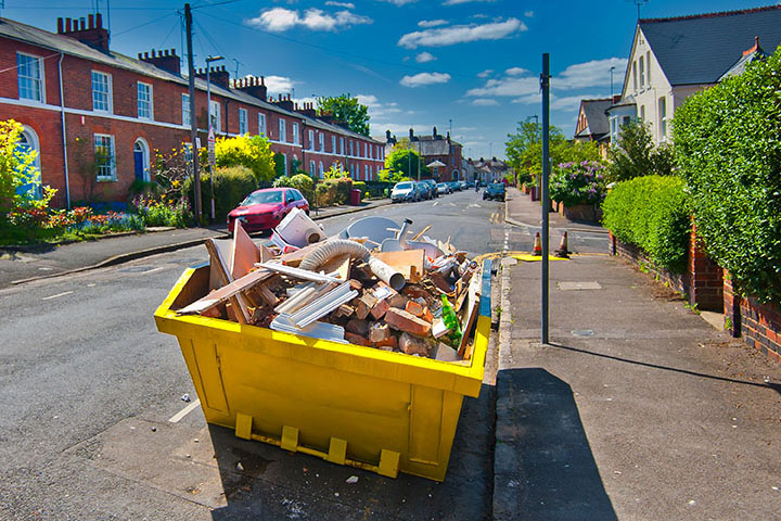 A yellow skip hire sitting on the side of a street.