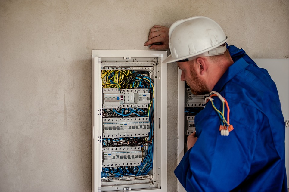 A man in a hard hat is working on an electrical panel, indicating the need for hiring an electrician.
