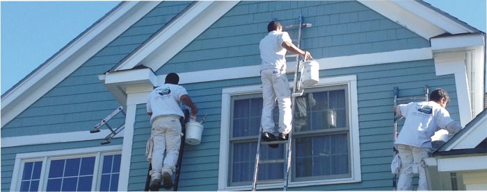 Three men improving curb appeal by painting a house on ladders.