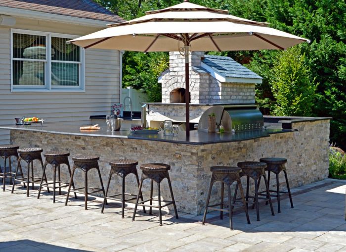 An outdoor kitchen with stools and an umbrella in a poolside backyard.