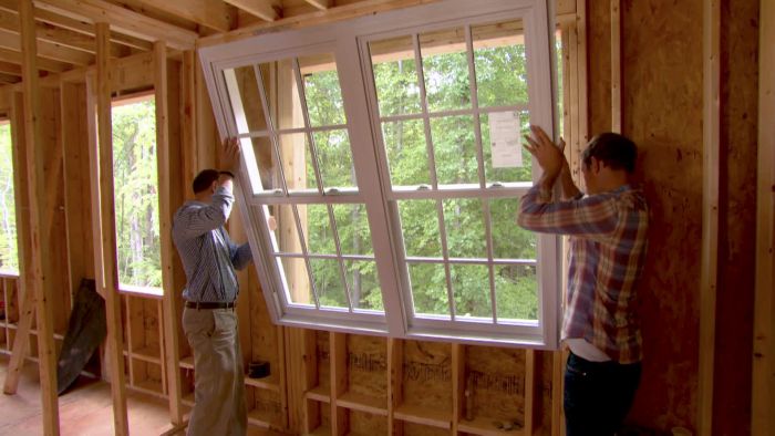 Two men undertaking a home improvement project by installing a window in an unfinished house.