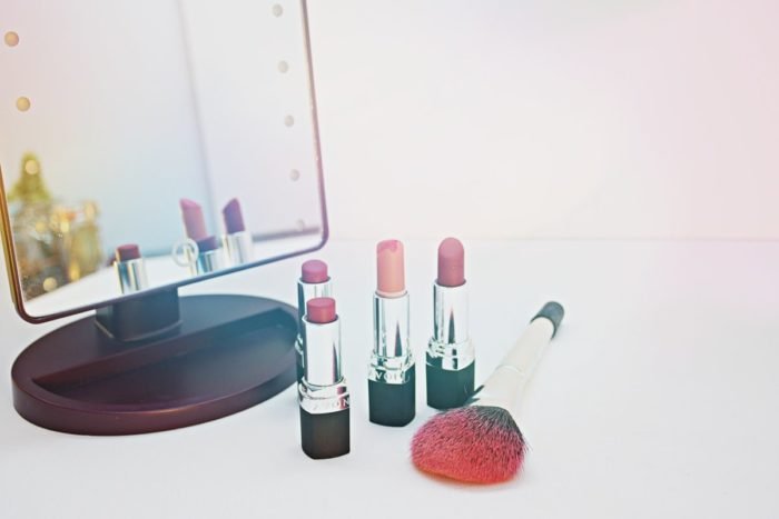 Makeup brushes and red lipstick in front of a mirror.
