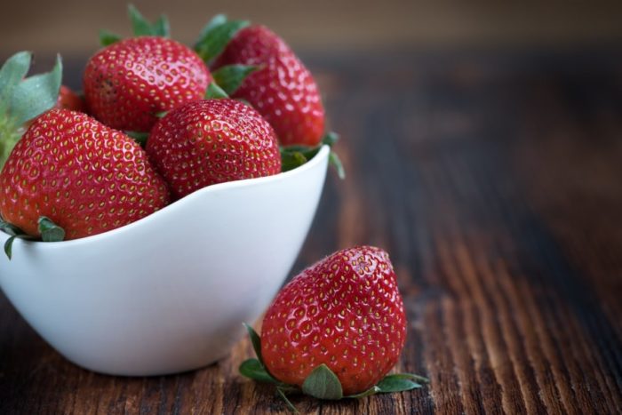 Strawberries with white teeth in a white bowl on a wooden table.