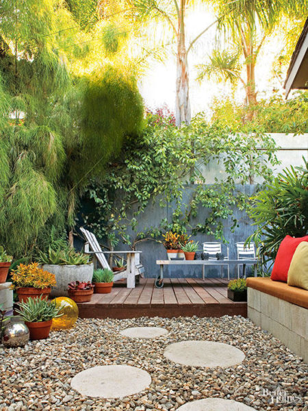 A small backyard with a gravel patio and plants in a garden.