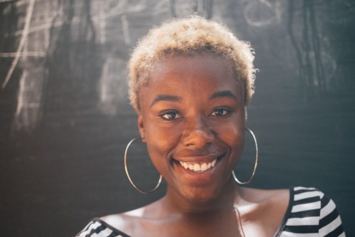 A young african american woman smiling in front of a blackboard while practicing double cleansing.