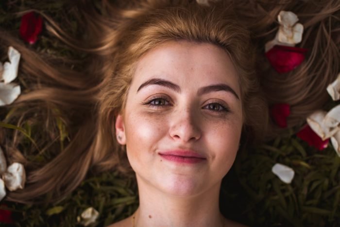 A young woman surrounded by rose petals, practicing double cleansing.