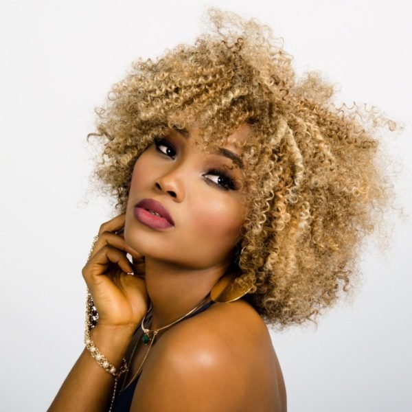 A woman with afro hair is posing for a photo with blush and bronzer.