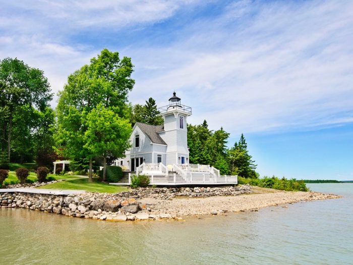 A white lighthouse sits on the shore of a body of water, serving as a home.