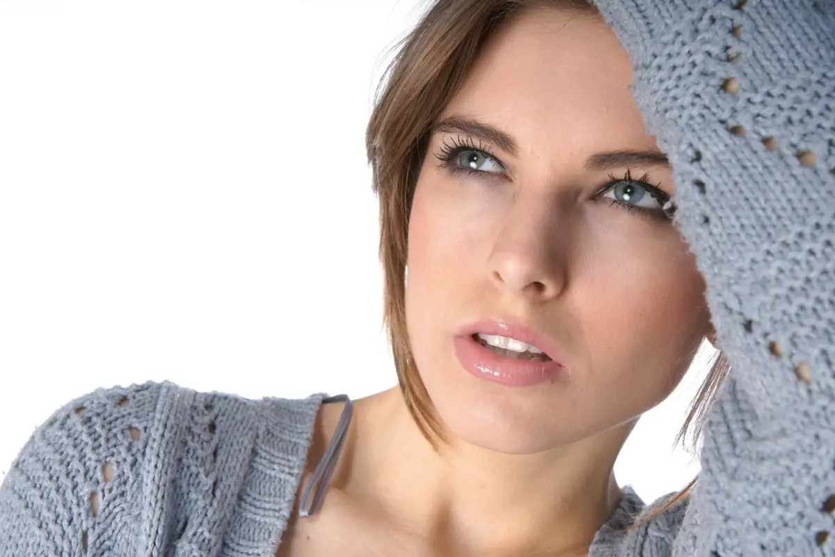 Woman in gray sweater looking upwards thoughtfully.