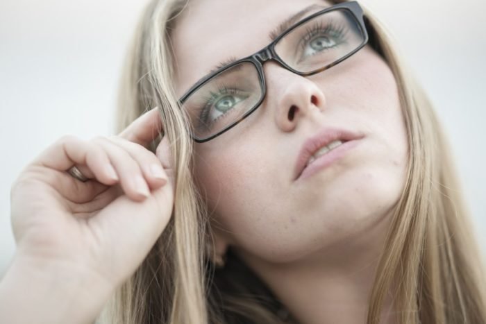A young woman wearing glasses is looking up at the sky with dark circles around her eyes.