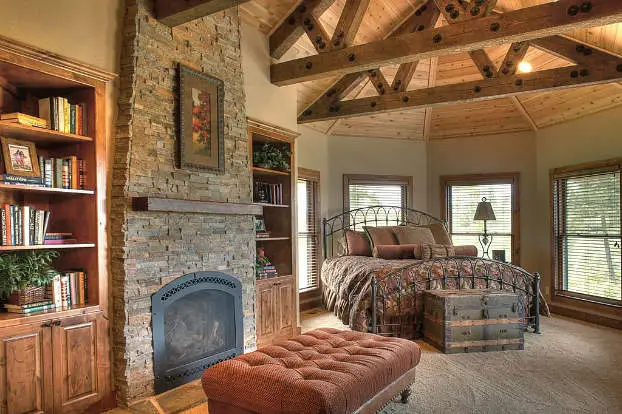 A cozy bedroom with a stone fireplace and wood beams.