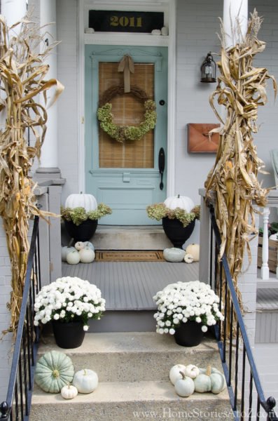 A front porch freshly decorated for fall with white pumpkins and corn.