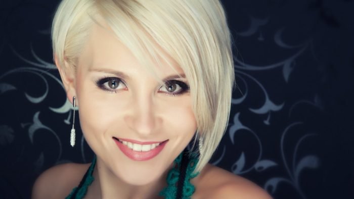 A woman with short blonde hair is smiling for the camera, gracefully avoiding beauty mistakes.