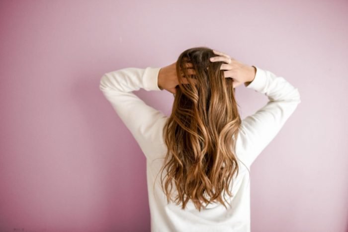 A woman with long hair standing in front of a pink wall, showcasing beauty.