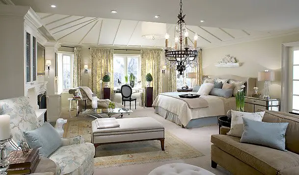 A cozy bedroom with a bed, couch, chairs and a chandelier.