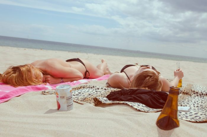 Two women enjoying a beach day with a bottle of beer.