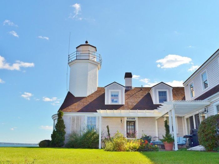 A lighthouse home sits on a lawn next to the ocean.