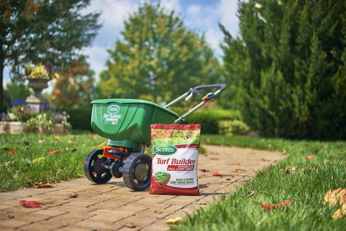 A lawn mower and a bag of fertilizer for lawn maintenance on a brick path.