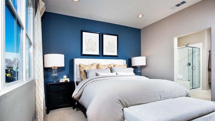 A bedroom with blue walls and a white bed that underwent a realistic extreme home makeover.