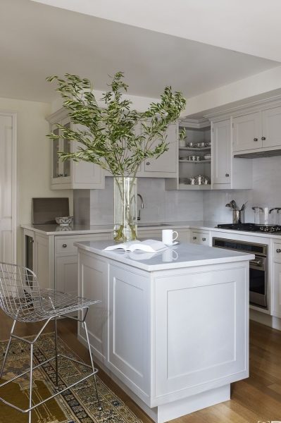 A small white kitchen with a white island and chairs.