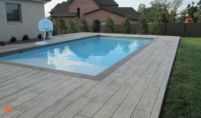A backyard pool with a wooden deck and a basketball hoop, utilizing stamped concrete for added appeal.