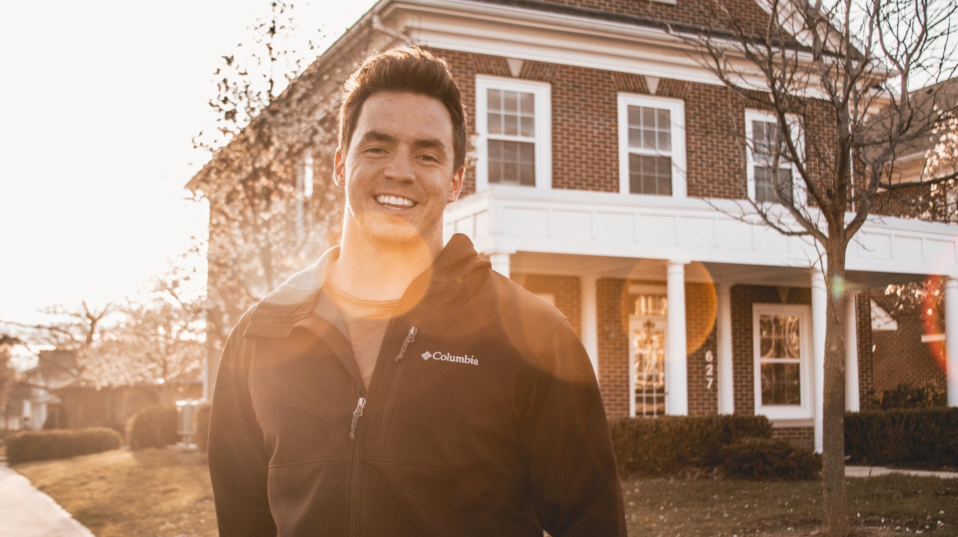 A man in a jacket standing in front of a house, potentially considering a home loan.