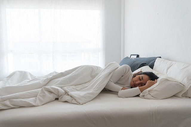 A woman improving her sleep on a white bed.