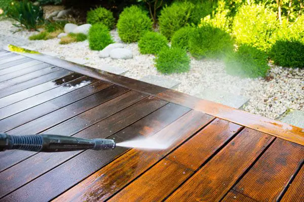 A man using a pressure washer to clean a composite deck.