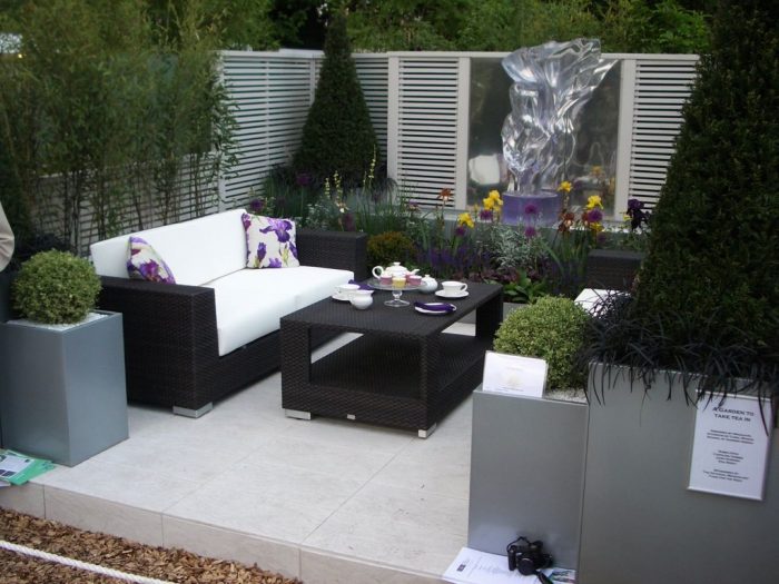 An outdoor garden with a white sofa, coffee table, and plants.