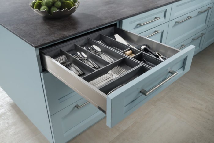 A blue kitchen with a drawer full of utensils, showcasing one of the top kitchen trends of 2019.