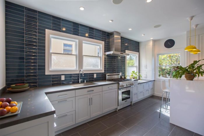 A trendy kitchen with blue tile and white cabinets.