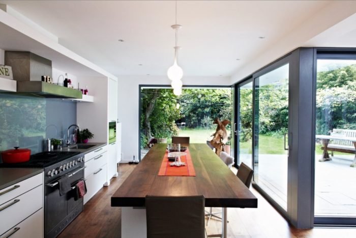 A modern kitchen featuring glass doors and a wooden table, highlighting two top kitchen trends of 2019.