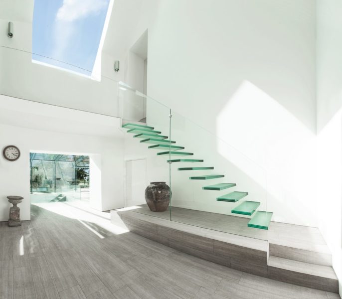 A glass staircase in a white house with skylights, perfect for an instant home update.