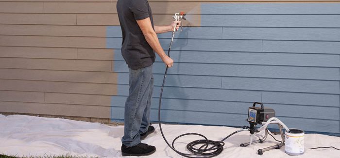 A man using a paint sprayer to guide painting a house.