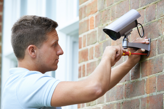 A man installing a home security camera on a brick wall.