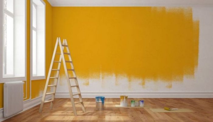 An empty room with yellow paint and a ladder in a painting profession setting.