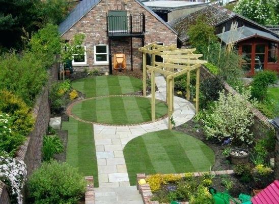 A small backyard with grass and a wooden deck, equipped with tools for gardening.