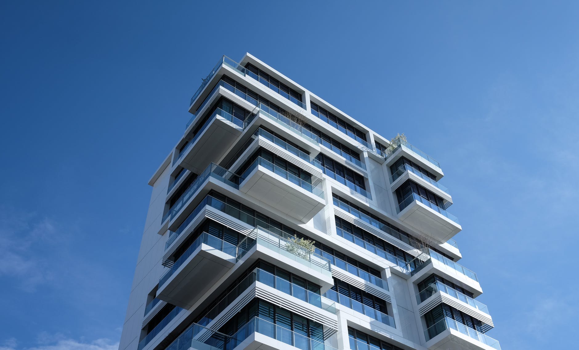 A modern building with balconies available for renting property against a blue sky.