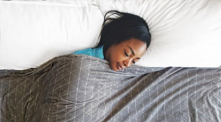 A woman sleeping in a bed with a weighted blanket over her head.