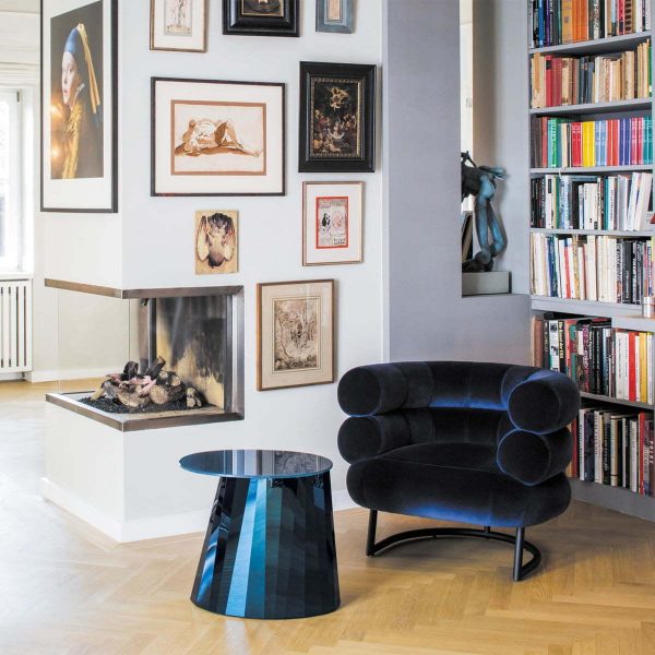 A living room with bookshelves and a blue chair, featuring the iconic Eileen Gray Bibendum Chair.