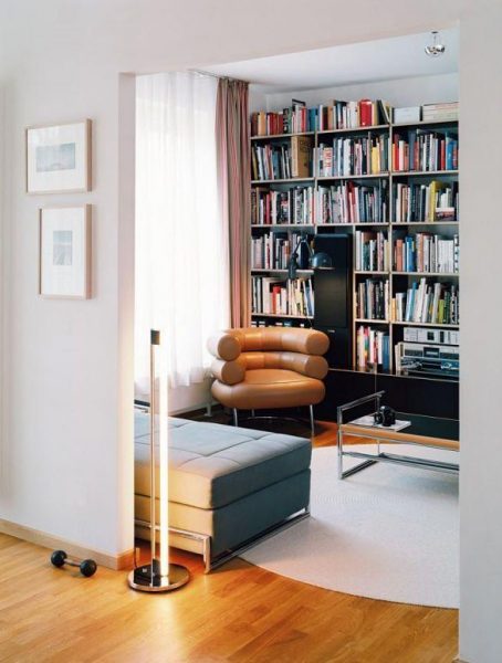A living room with bookshelves, a couch, and Eileen Gray Bibendum Chair.