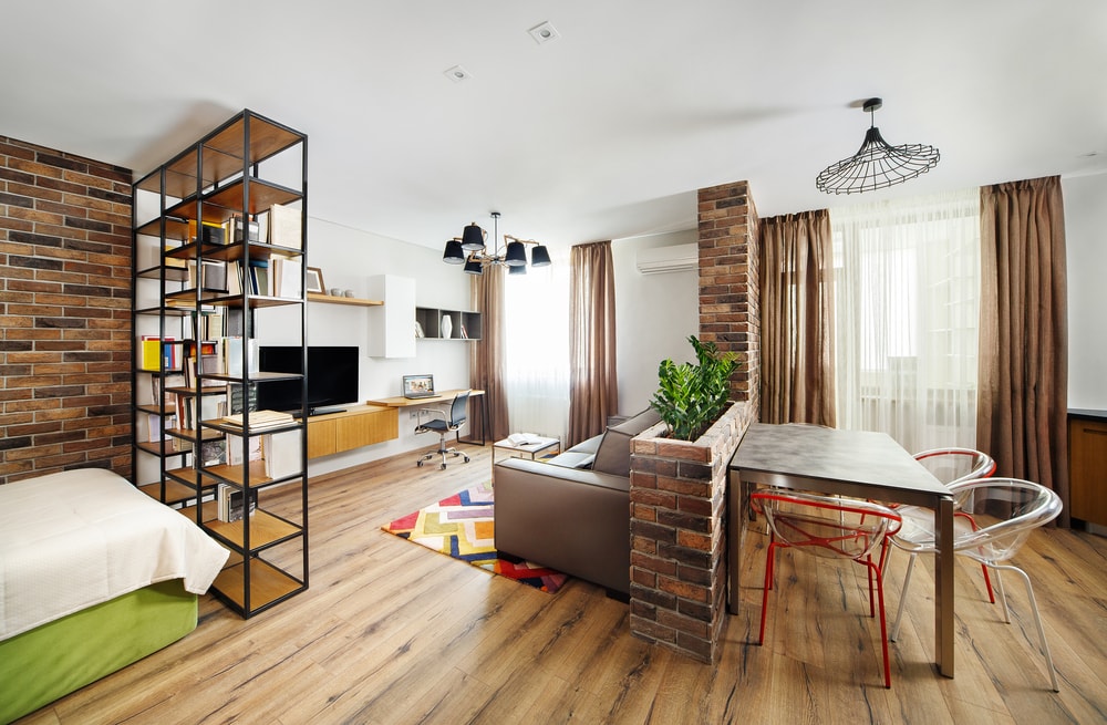 A small studio apartment with wooden floor and brick walls.