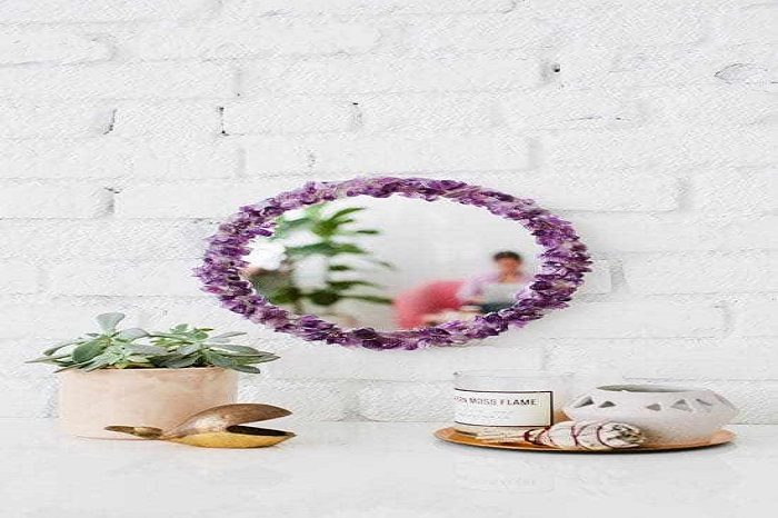 A purple mirror with a personal touch on a white wall next to a potted plant.