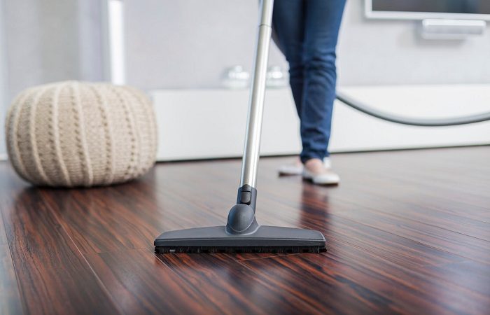 A woman cleaning a hardwood floor in a living room.