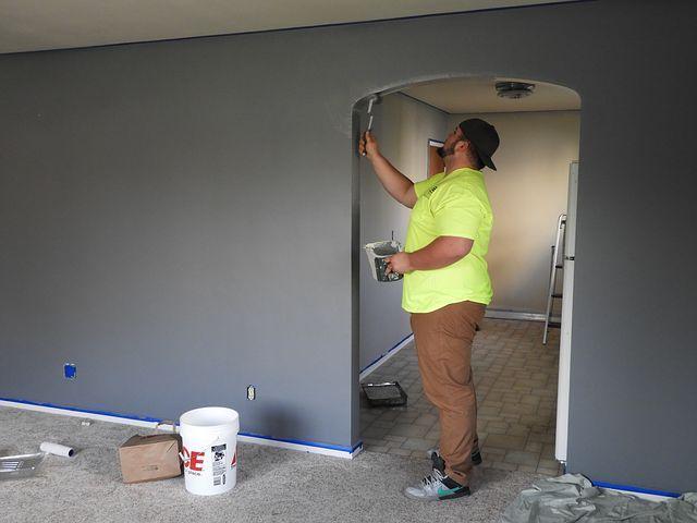 A man renovating a home by painting the walls gray.