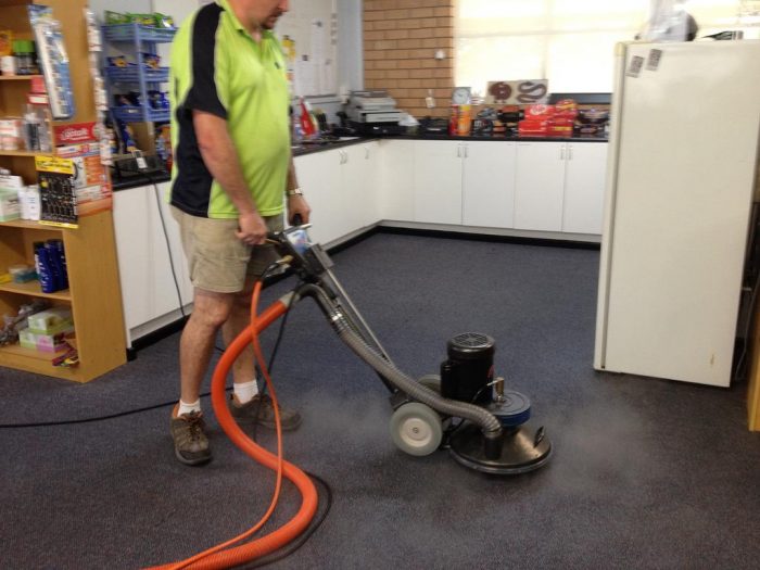 A professional using a carpet cleaning machine in a kitchen.